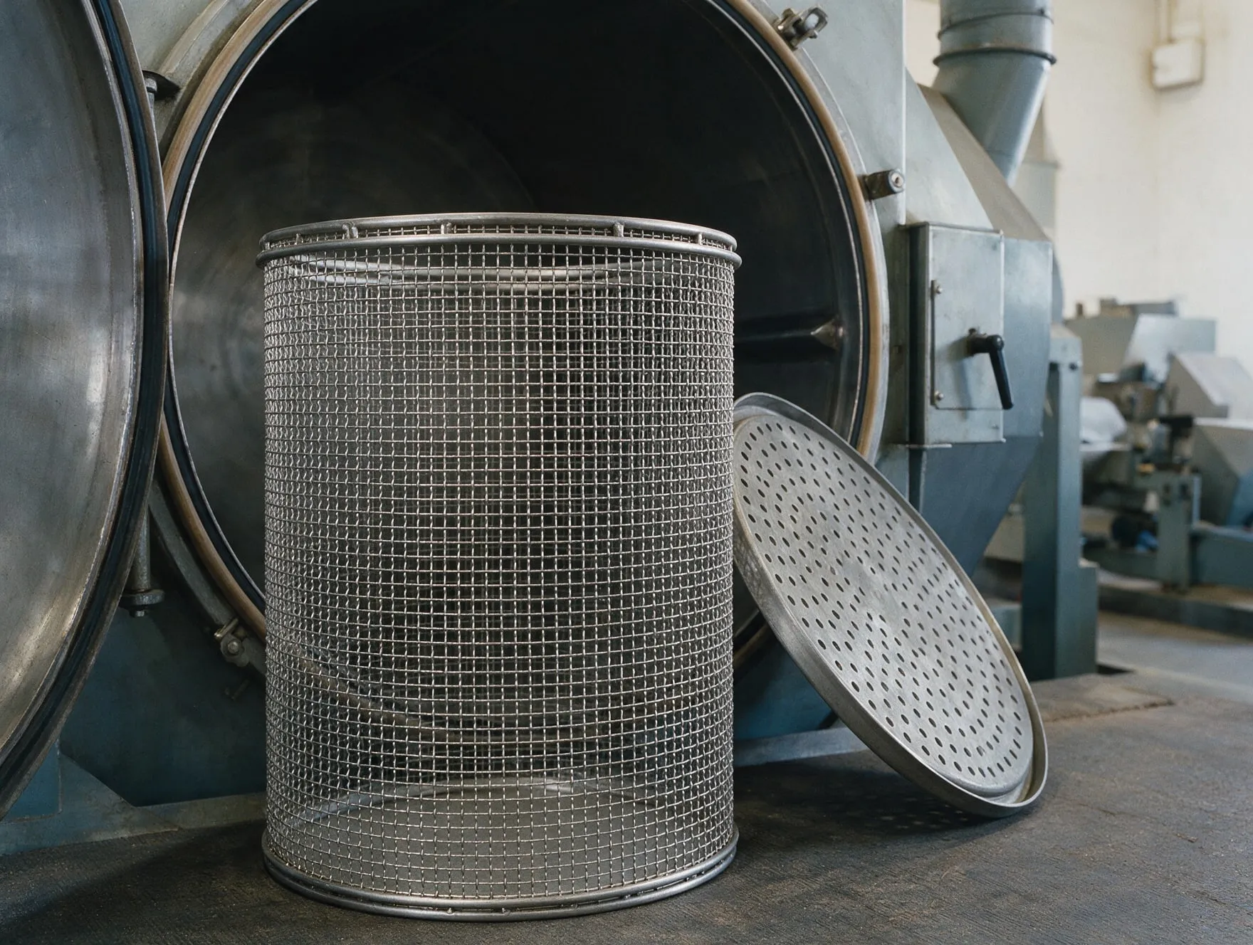 A wire mesh dryer basket and a perforated fluidizing bottom plate beside an open industrial dryer